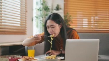 Genç bir kadın kanepede spagetti yiyor, gülüyor, evde yemeğin tadını çıkarıyor..