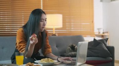 Ev hayatı, insanlar ve yemek konsepti. Pizza yiyen ve oturma odasında laptop kullanan çekici bir kadın..