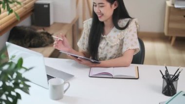 Güzel, neşeli genç bir kadın dizüstü bilgisayardan bilgi alıyor ve dijital tablet üzerinde yazıyor..