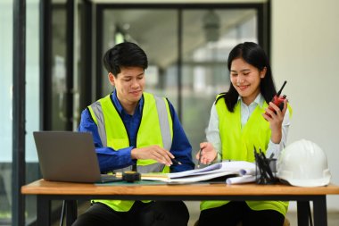 Sarı yelekli iki mühendis ve kadın ofiste yeni projeyi tartışıyorlar.