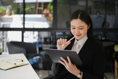 Siyah takım elbiseli çekici Asyalı kadın girişimci dijital tablet kullanıyor, ofiste online veri pazarı analizi yapıyor...