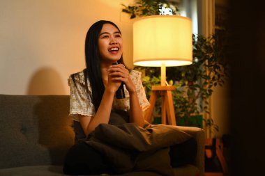 Televizyon izleyen mutlu bir kadın ve oturma odasındaki kanepede uzaktan kumandayla. Eğlence, rahatlama ve boş zaman aktivitesi..