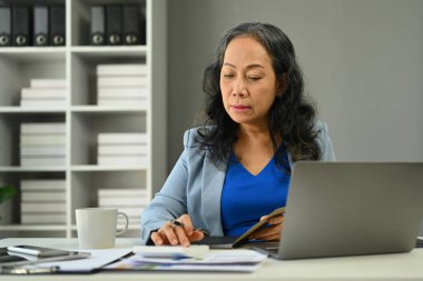 Modern ofiste istatistik belgeleriyle çalışan başarılı bir orta yaşlı iş kadını...