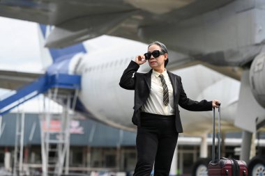 60 'ların takım elbiseli ve güneş gözlüklü iş kadını uçağın yanında duruyor. İş seyahati ve ulaşım..