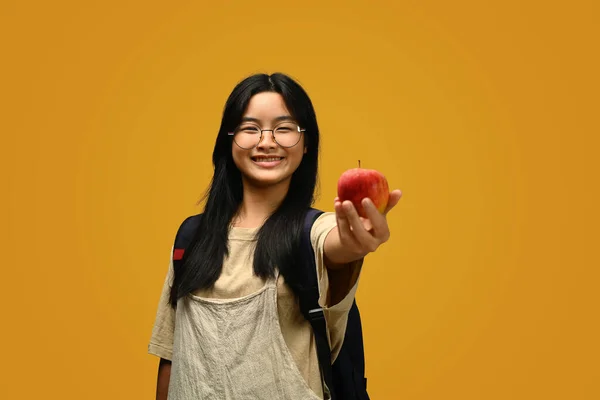 黄色の背景にリンゴをかぶったメガネをかぶったハッピーな女子高生 そして学校のコンセプトに戻る — ストック写真