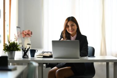 Modern işyerinde oturan ve dizüstü bilgisayar kullanan bin yıllık kadın sekreterin portresi..