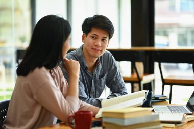 Asyalı erkek ve sınıf arkadaşı masada oturmuş sınavlara hazırlanıyor ve üniversite ödevleri için bilgi topluyorlar..