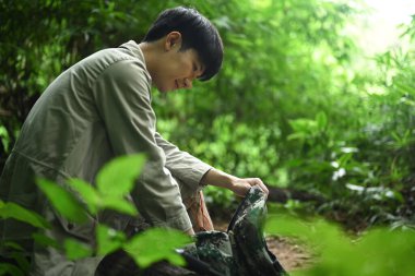Yeşil ormanda yürüyüş yaparken sırt çantalı bir adam kayaların üzerinde dinleniyor. Seyahat, yürüyüş ve macera konsepti.