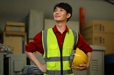 Karton kutu yığınının yanında duran güvenlik yeleği giyen yakışıklı bir depo çalışanı..