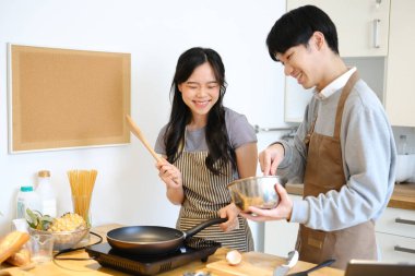 Önlüklü genç Asyalı çift kahvaltı için krep yapıyor, hafta sonunu birlikte geçiriyorlar..