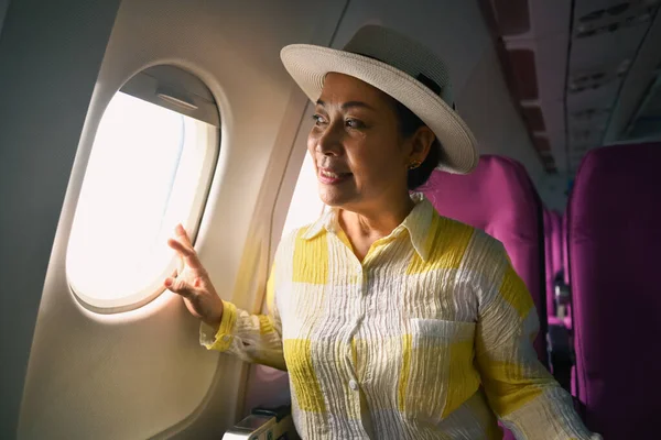 Positive middle age female tourist looking through airplane window. Retirement, travel and summer vacation concept.