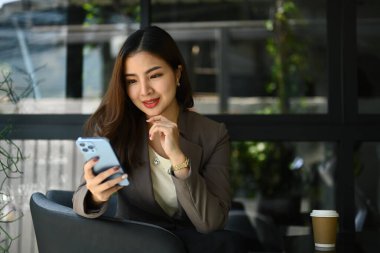 Kafede oturan çekici iş kadını, akıllı telefondan mesajları ya da sosyal medyayı kontrol ediyor..