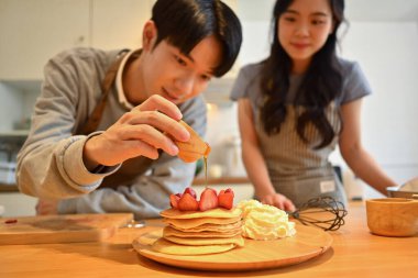 Adam, ahşap mutfak masasında çilekli lezzetli kreplere bal döküyor..