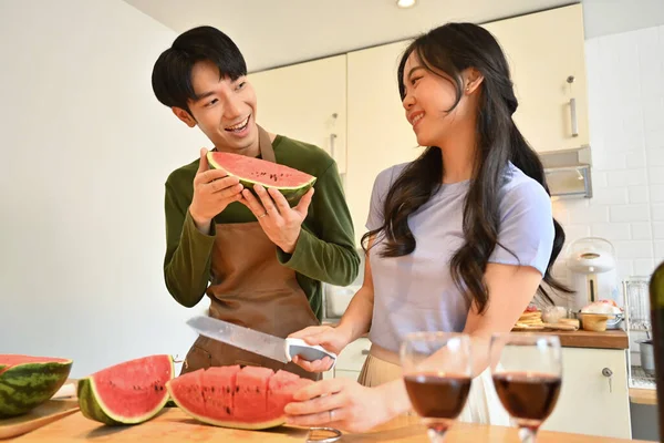 木製のキッチンタブレットの後ろに立っているエプロンで幸せな夫婦と甘いスイカを食べる — ストック写真