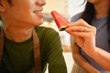 Güzel Asyalı bir çiftin mutfakta durması, genç bir bayanın erkek arkadaşını karpuzla beslemesi. İlişki, ev hayatı kavramı.