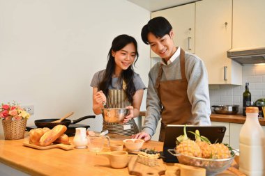 Güzel genç bir çift mutfakta yemek pişiriyor ve dijital tablette online bir tarifi takip ediyor..