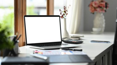 Rahat iş yeri, boş ekranlı dizüstü bilgisayar, evraklar ve hesap makinesi beyaz masa üzerinde.