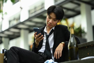 Sarhoş ya da alkolik iş adamı merdivenlerde oturmuş bira içiyor ve kovulduktan sonra telefon kullanıyor. İş kaybı, işsizlik.