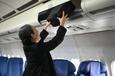 Gülümseyen orta yaşlı kadın yolcular bavullarını bir uçaktaki kompartımana koyuyorlar..