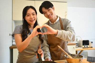 Güzel, genç, evli bir çift mutfakta duruyor, elleriyle kalp şekillendiriyorlar ve kameraya gülümsüyorlar..