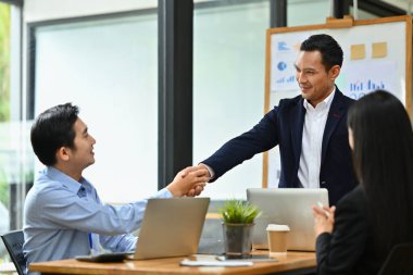 Arkadaş canlısı erkek yönetici, toplantı ve başarı projesinden sonra iş arkadaşıyla tokalaşıyor..