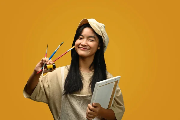 可爱的少女拿着画布和黄色背景的画笔 创意和教育概念 — 图库照片