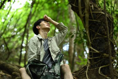 Sırt çantalı yorgun bir gezgin ormanda yürüyüş yaparken kayaların üzerinde dinleniyor. Seyahat, yürüyüş ve macera konsepti.