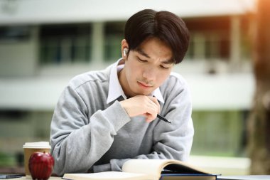 Konsantre Asyalı erkek öğrenci kitap okuyor, sınava hazırlanıyor ya da parkta ödev yapıyor..
