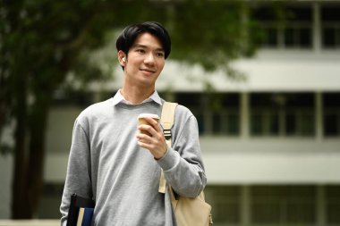 Kitap ve kağıt bardakla kampüsün önünde duran mutlu genç üniversite öğrencisi. Eğitim ve yaşam tarzı kavramı.