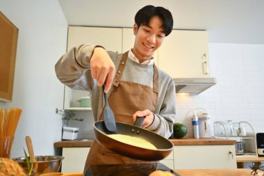 Genç Asyalı adamın mutfakta kahvaltı hazırlarken spatulayla sıcak krep fırlatması..