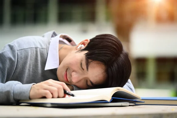 Asian male university student fallen asleep on his textbook, being exhausted during preparing for exams.