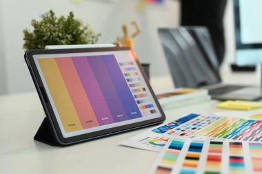 Yaratıcı tasarımcı, dijital tablet, renk örnekleri ve ahşap masadaki kırtasiye malzemeleriyle çalışma alanında grafiksel çizim.