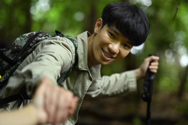 Yakışıklı erkek gezgin, arkadaşının ormanda kayaya tırmanmasına yardım ediyor. Seyahat, yürüyüş ve macera konsepti.