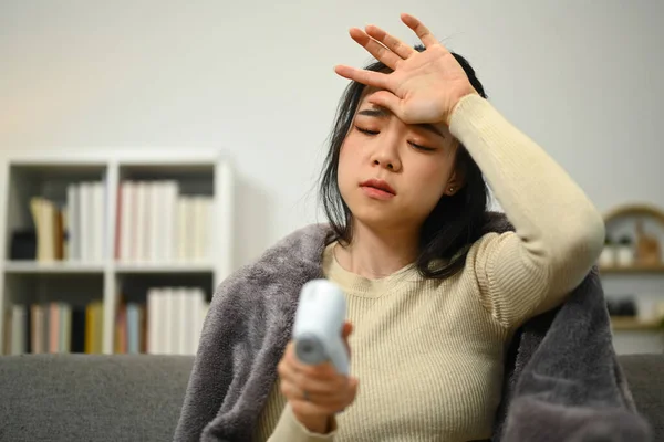 Młoda Kobieta Mierzy Gorączkę Termometrem Podczerwień Dotyka Czoła Siedząc Kanapie — Zdjęcie stockowe