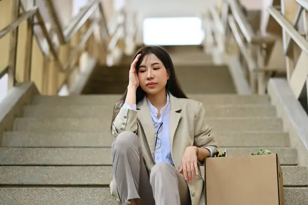 Fired businesswoman sitting hopelessly sitting on stairs of a business building. unemployment, depressed and fired from job.