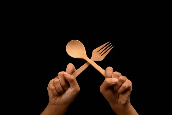Hands holding spoon and fork over black background. Gesture of eating, dinning and cooking.