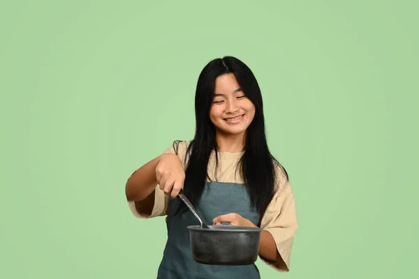 穿着围裙 拿着绿色背景的锅子和铲子 微笑着的少女 — 图库照片