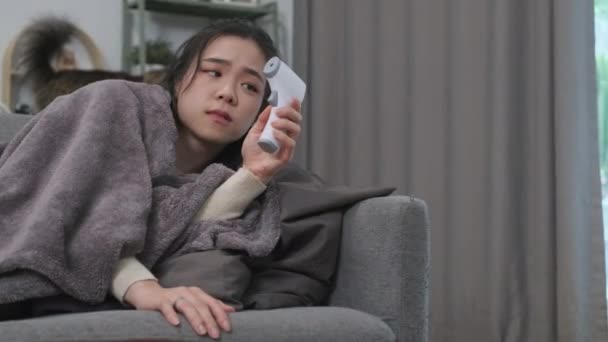 ソファーに横たわり 赤外線温度計で熱を測定する毛布の若い女性 医療コンセプト — ストック動画