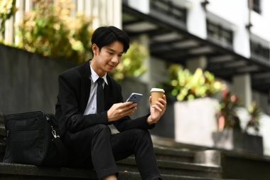 Takım elbiseli yakışıklı bir işadamı akıllı telefon kullanıyor, binanın merdivenlerinde oturuyor..