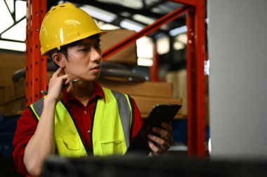 Raflarla dolu perakende deposunda duran ve panoda malzeme ihracatını kontrol eden bir erkek işçi..