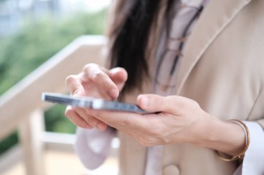 İş kadınının cep telefonuyla mesajlaşırken, dışarıda müşteriyle sohbet ederken görüntüsü kesilmiş. Teknoloji ve şehir hayatı kavramı.