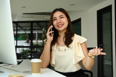 Güzel Asyalı kadın girişimci iş yerinde oturup hoş bir telefon görüşmesi yapıyor..