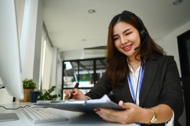 İyi, arkadaş canlısı kadın satış danışmanı. Kulaklıkla müşteriyle konuşuyor ve kâğıt üzerinde notlar alıyor..