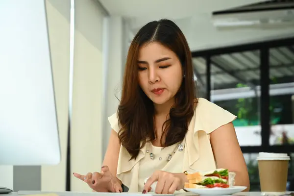 漂亮的年轻女商人在办公室用电脑吃饭时吃三明治 — 图库照片