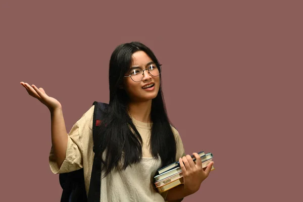 アジアの女子高生は紫色の背景の上に教科書を持っているメガネを身に着けています そして学校のコンセプトに戻る — ストック写真