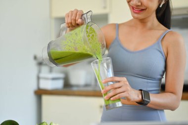 Spor elbiseli genç bir kadın cama smoothie döküyor. Diyet ve sağlıklı yaşam tarzı kavramı.