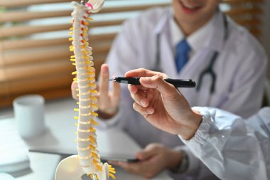 Ortopedist beyaz laboratuvar önlüğü, omurga modelini gösteren hasta tedavisini tartışıyor..