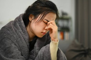 Hasta Asyalı kız gri battaniyeye sarılıp gözlerine masaj yapıyor, migren belirtileri gösteriyor ya da baş ağrısı çekiyor..