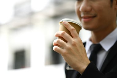 Gülümseyen işadamı gece sokaklarda yürürken kağıt bardaktan kahve içiyor..