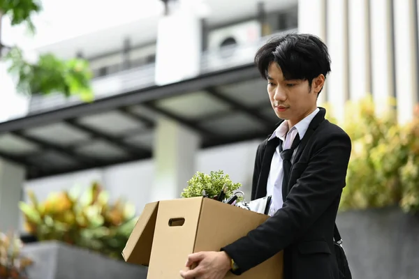 Unemployed, quit job. Young businessman holding cardboard box with belongings resigning from company.